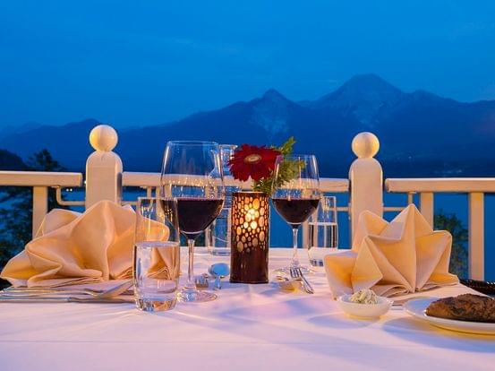 Romantisches Abendessen mit Wein und Kerzenblick auf Berge und See bei Sonnenuntergang